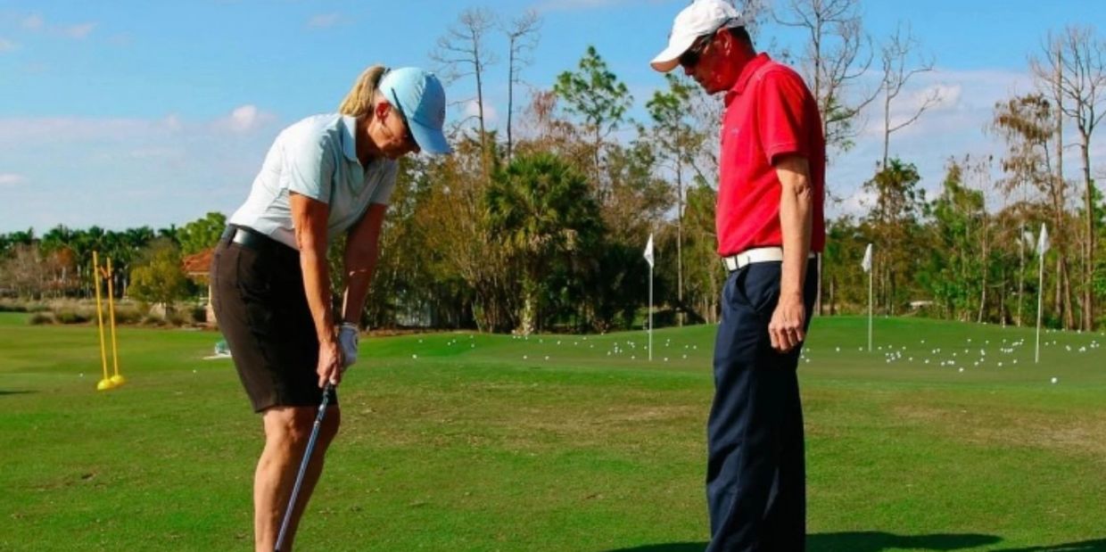 Two people on golf course, one preparing to putt.