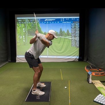 Man practicing golf swing indoors with a golf simulator.