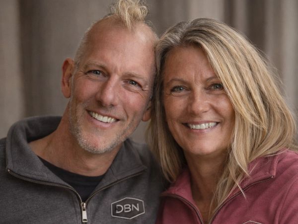 Smiling couple wearing matching DBN zip-up sweaters, close and happy.