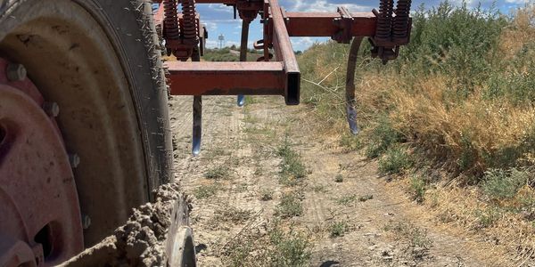 Close-up of a muddy farm tractor wheel and attached rusted cultivator under a partly cloudy sky.