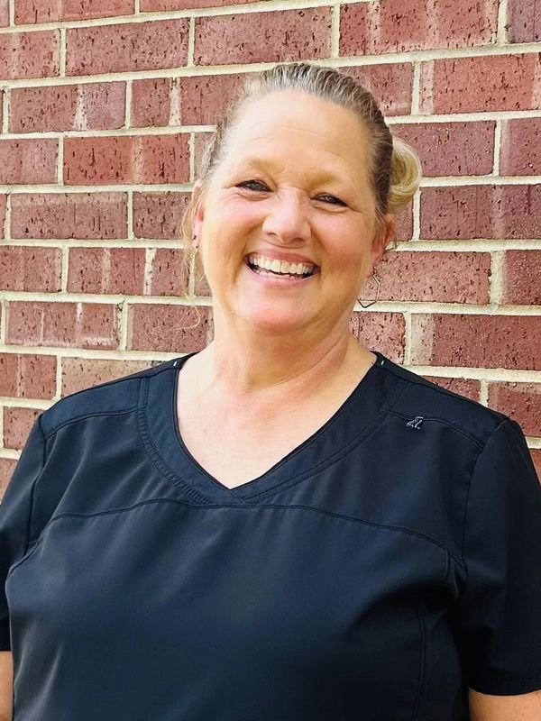 Smiling woman in black shirt standing against a brick wall.