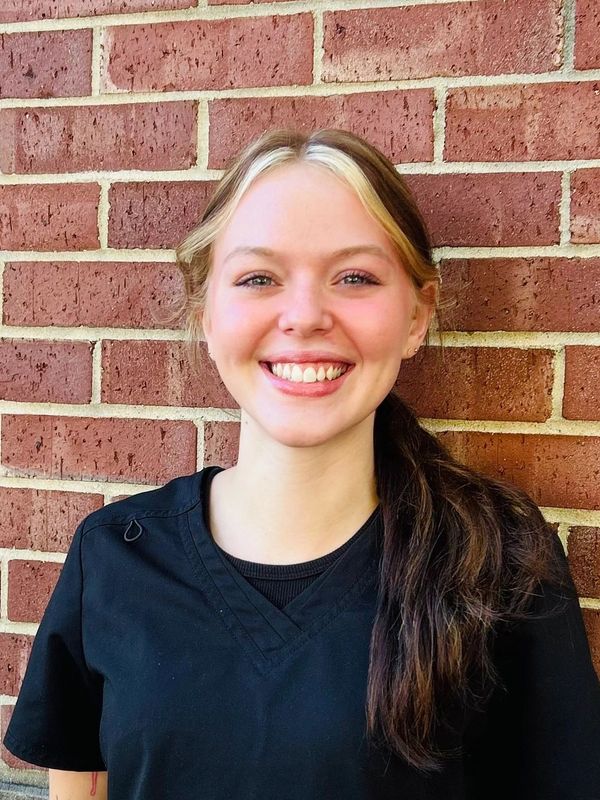 Smiling young woman in black scrubs against a brick wall.