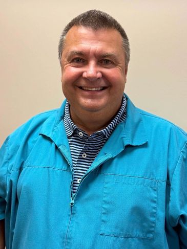 Smiling man in a blue jacket stands against a plain background.