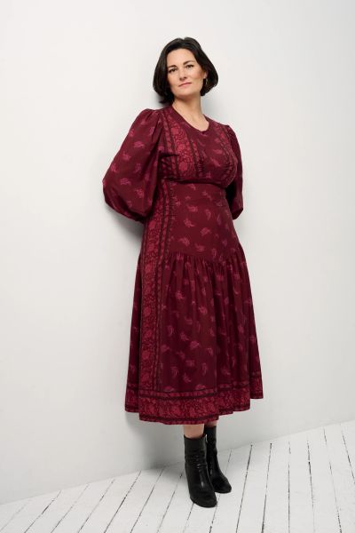 Woman in a burgundy floral dress with puff sleeves and black boots.