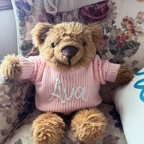 A teddy bear wearing a pink sweater with the name Ava on it.