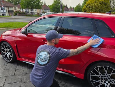 Man cleaning red car with cloth.