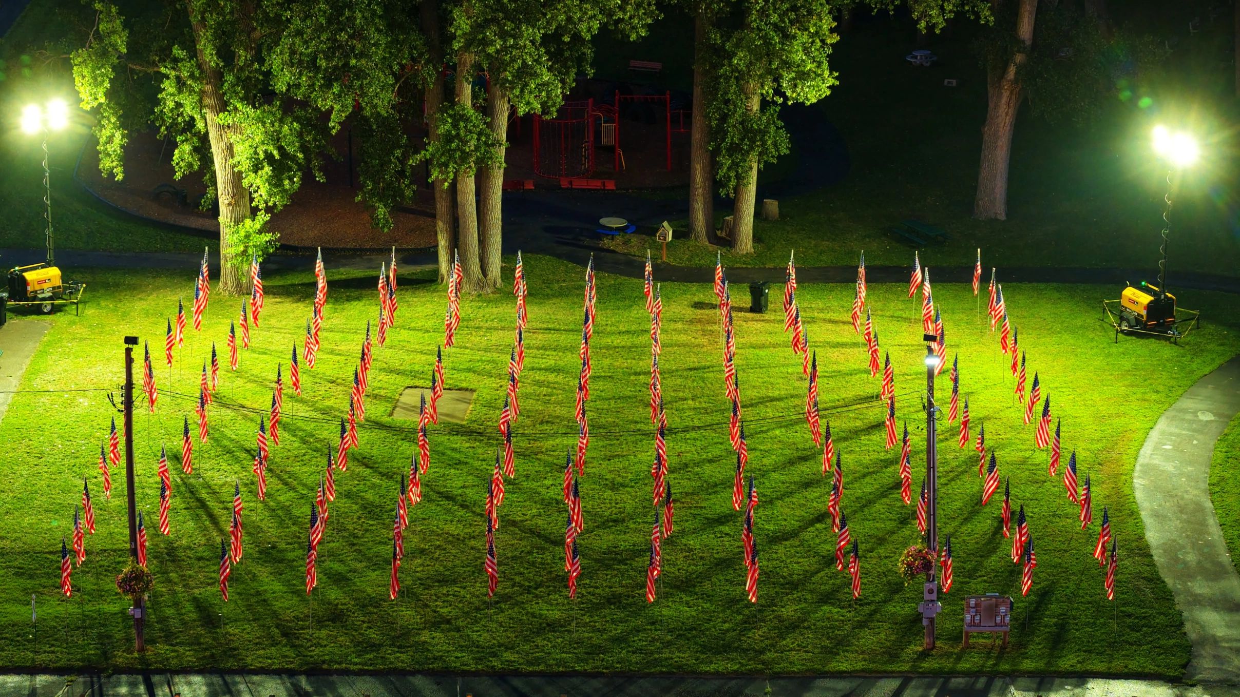 Rows of American flags illuminated at night in a park.