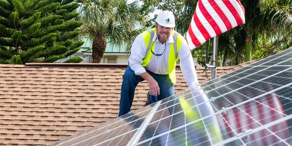 A man wearing a white helmet crouching to the solar panels