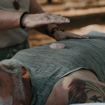 A person performing crystal healing on a tattooed man lying down.