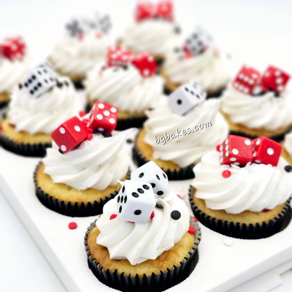 Cupcakes with white frosting topped with red and white dice decorations.