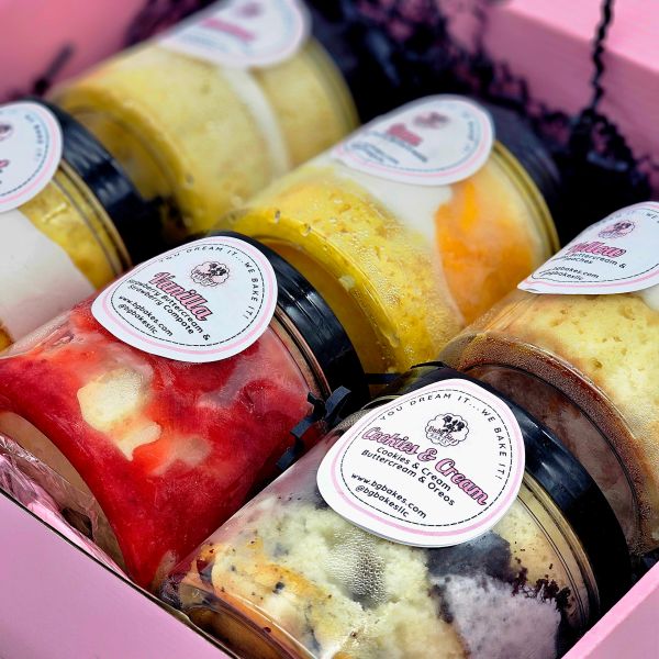 Assorted jarred desserts with labels in a pink box.