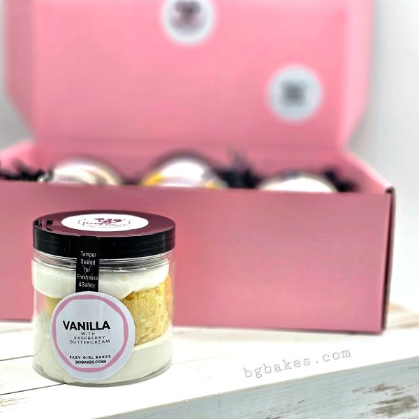 A vanilla cake jar with raspberry buttercream in front of a pink box.