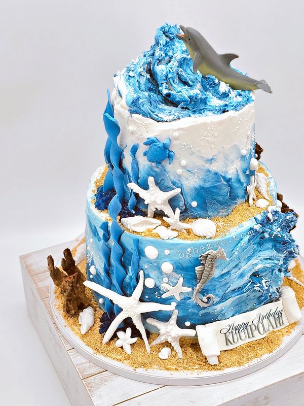 Two-tier ocean-themed cake with marine decorations and a dolphin topper.