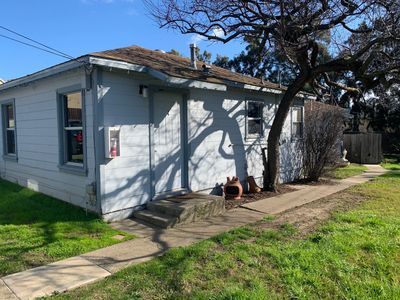 Small white house with a tree casting shadows on the wall under a clear blue sky.
