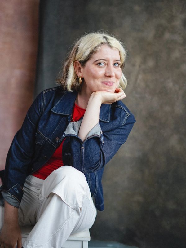 Woman with blonde hair in denim jacket posing with a smile.