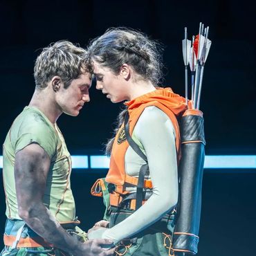 Two archers sharing a close, intense moment holding hands on stage.