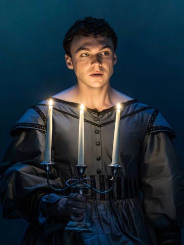 A young man holding a candelabrum with lit candles in a dark setting.