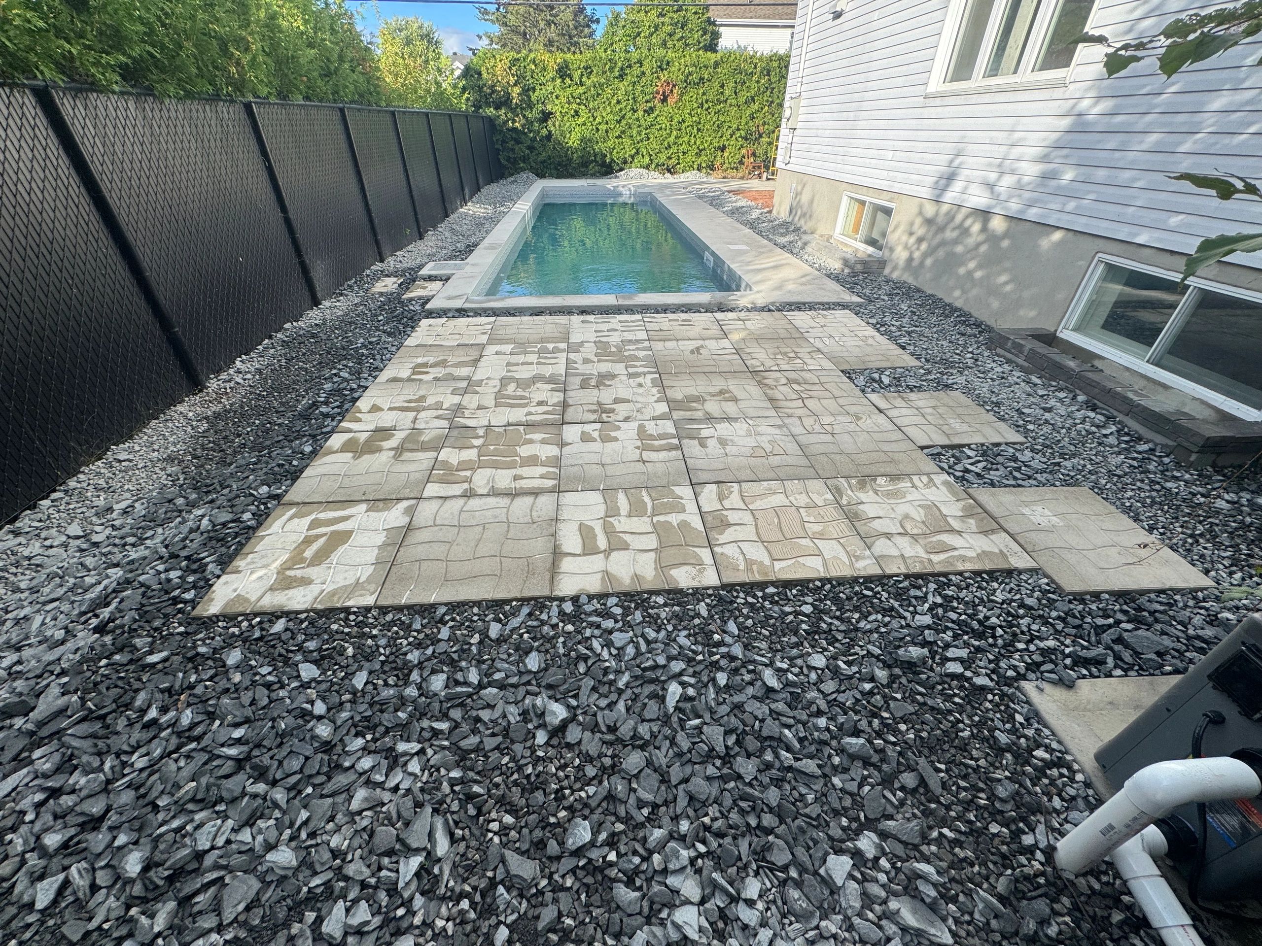 Piscine rectangulaire dans une cour arrière avec dalles et gravier.