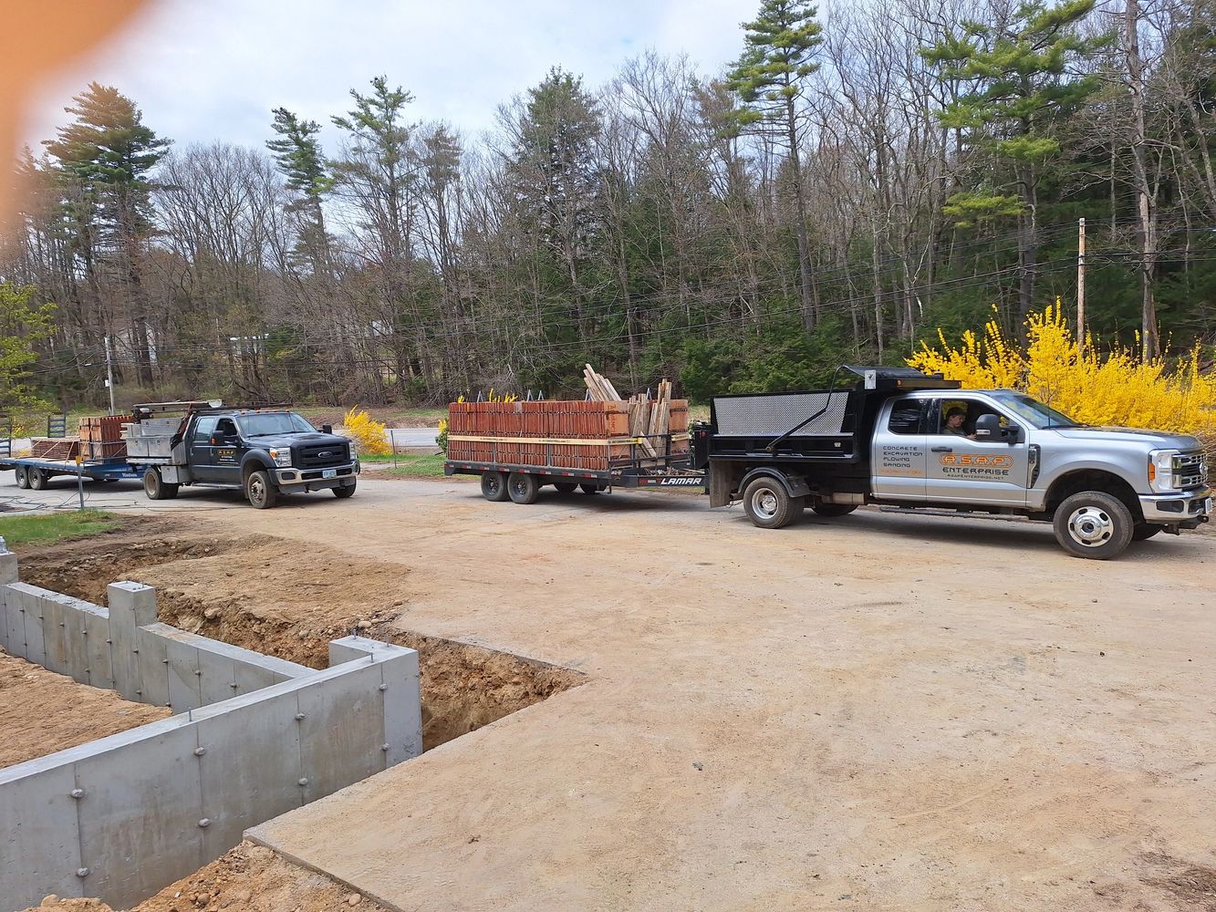 Two trucks with trailers loaded with wooden stakes at a construction site.