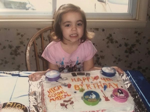 A young girl smiles behind her decorated 4th birthday cake.