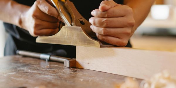 Person using a hand plane to smooth wood on a workbench.