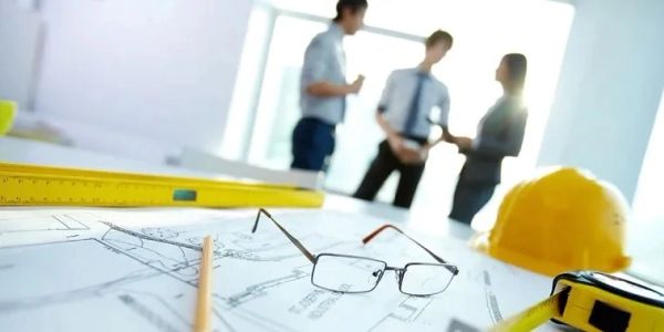 Architectural plans with tools and professionals in background.