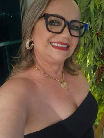 Mulher sorridente com óculos e vestido preto.