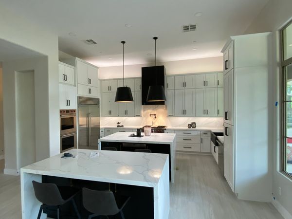 Modern kitchen with white cabinets, marble countertops, and black pendant lights.