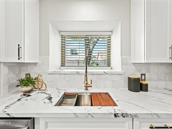 Modern white kitchen sink with marble countertops and gold faucet.