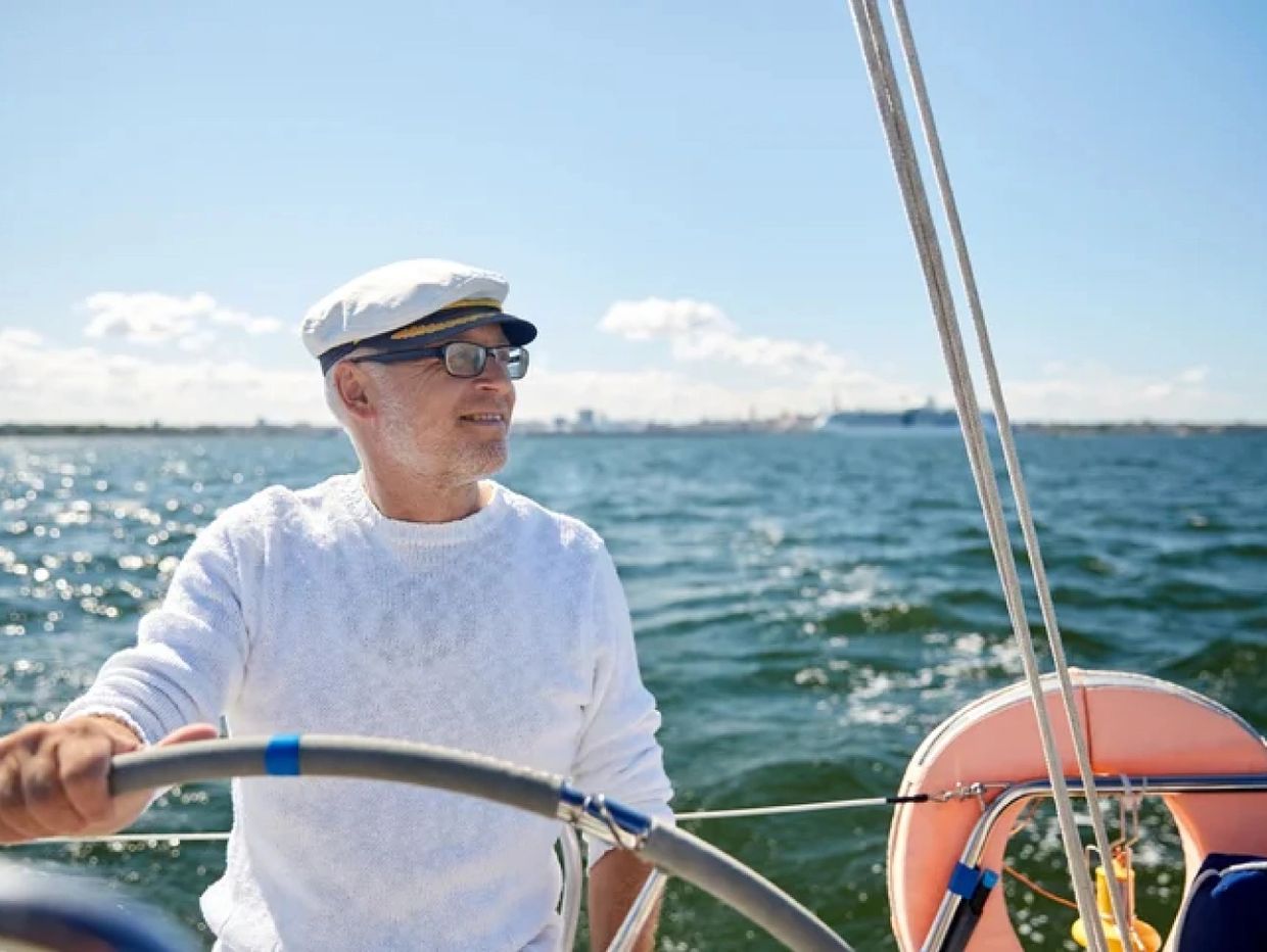 Elderly man steering a sailboat on a sunny day.