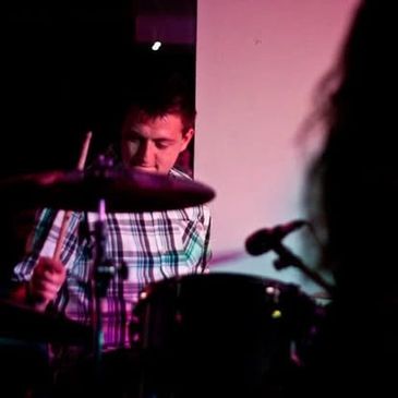 A man playing drums in a dimly lit setting with colorful lighting.
