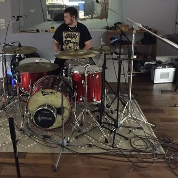 Drummer in a studio surrounded by drums and microphones.