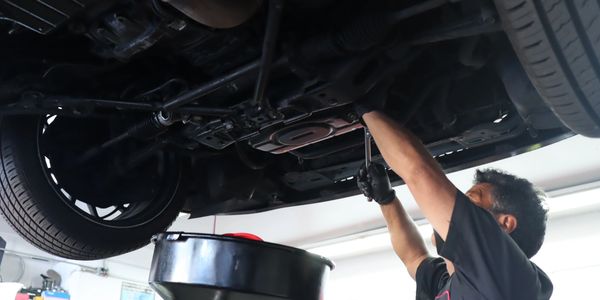 Mechanic under vehicle performing an oil change job. Tires are visible and tire rotation is next. 
