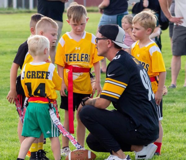 Coach talks to kids in Steelers jerseys on football field.