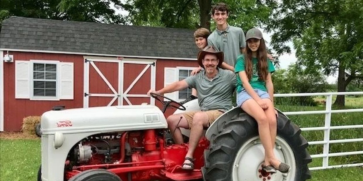 A family of four posing on a vintage Ford tractor in front of a red barn.
