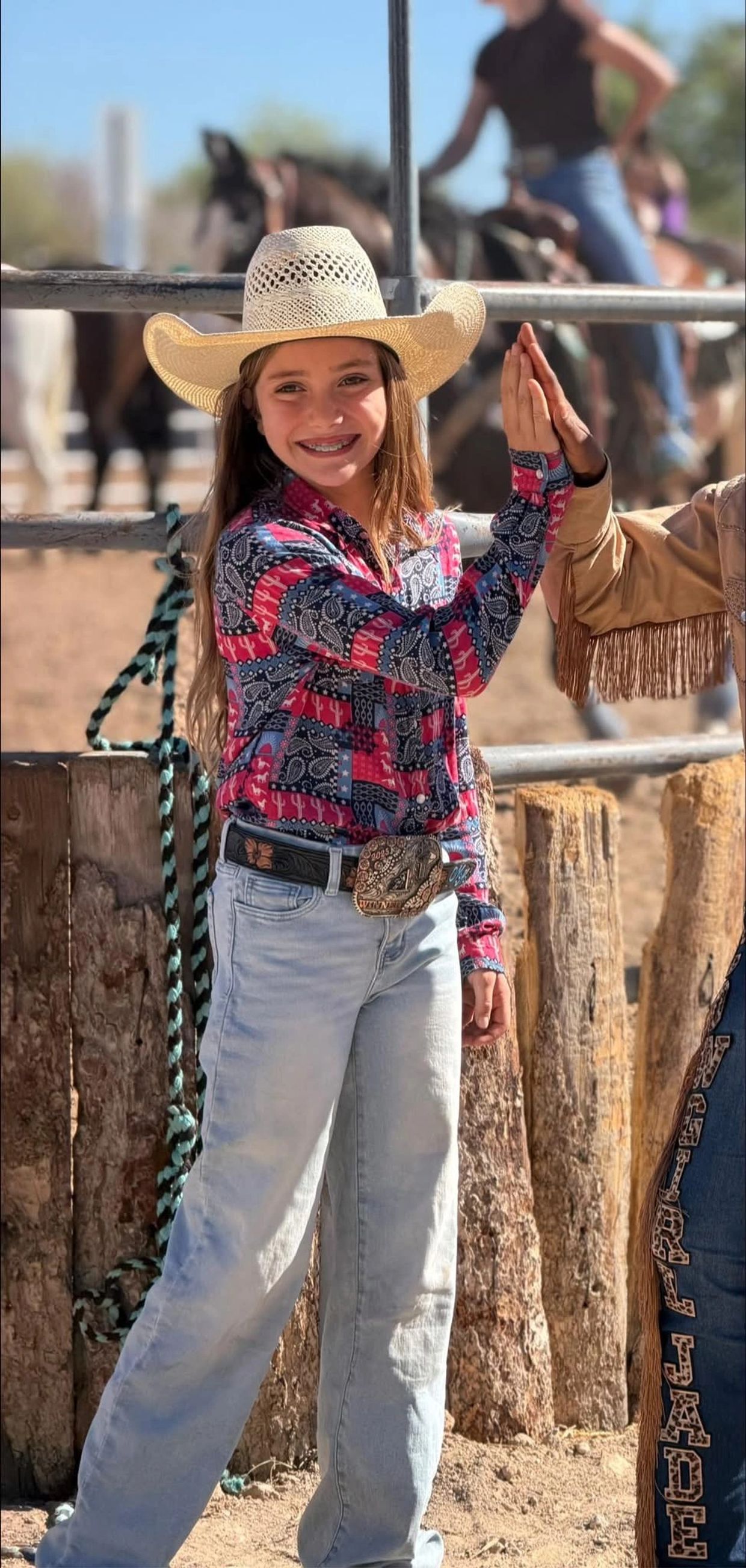 Young girl in cowboy attire giving a high five at a rodeo.