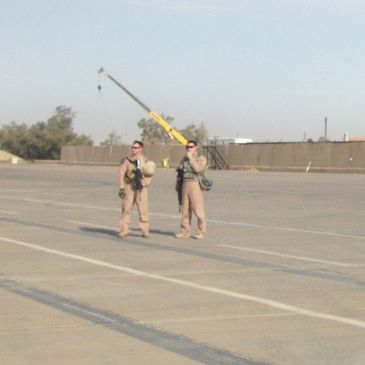 Two soldiers standing on a large concrete surface near a crane.