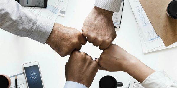 Four office workers fist bumping over a desk with files, coffee cup, i-phones and stationery on the 