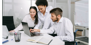 Asian woman, Black woman and White man in a wheelchair looking at a computer