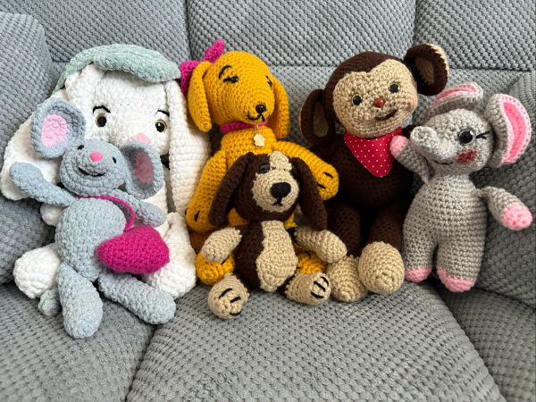 Five crocheted animal stuffed toys sitting on a grey textured sofa.