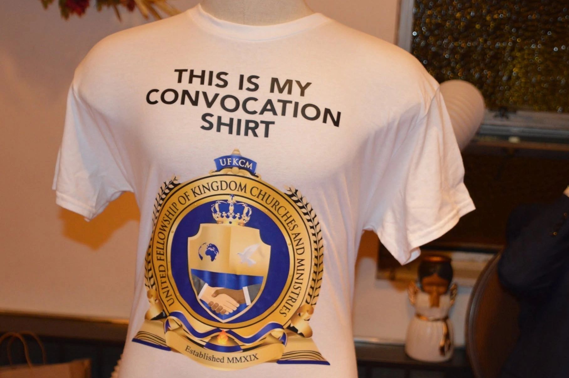 White convocation shirt with a church emblem and bold text.