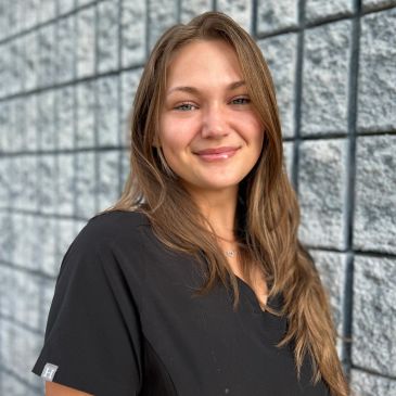 Smiling woman in black top against stone wall.