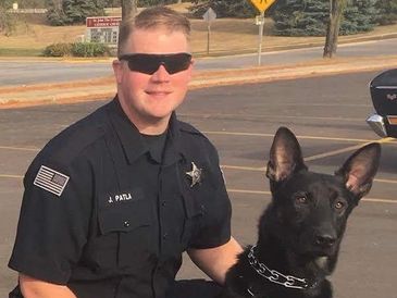 Police officer posing with a black police dog in a parking lot.