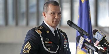 Military officer speaking at a press conference with microphones.