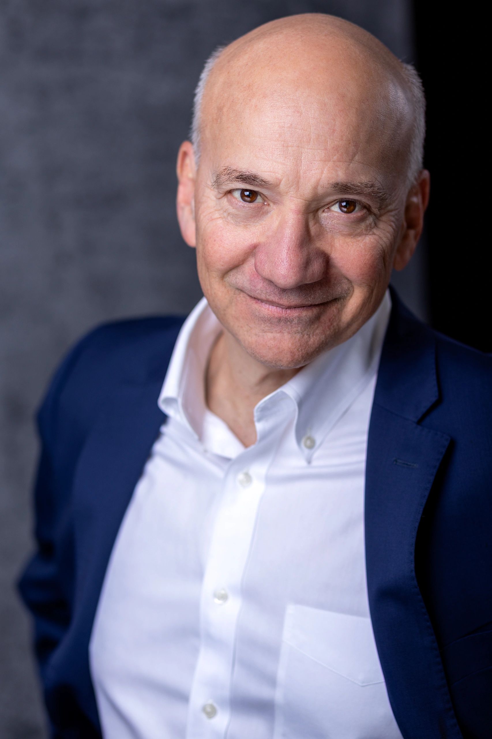 Smiling bald man in a navy blazer and white shirt.