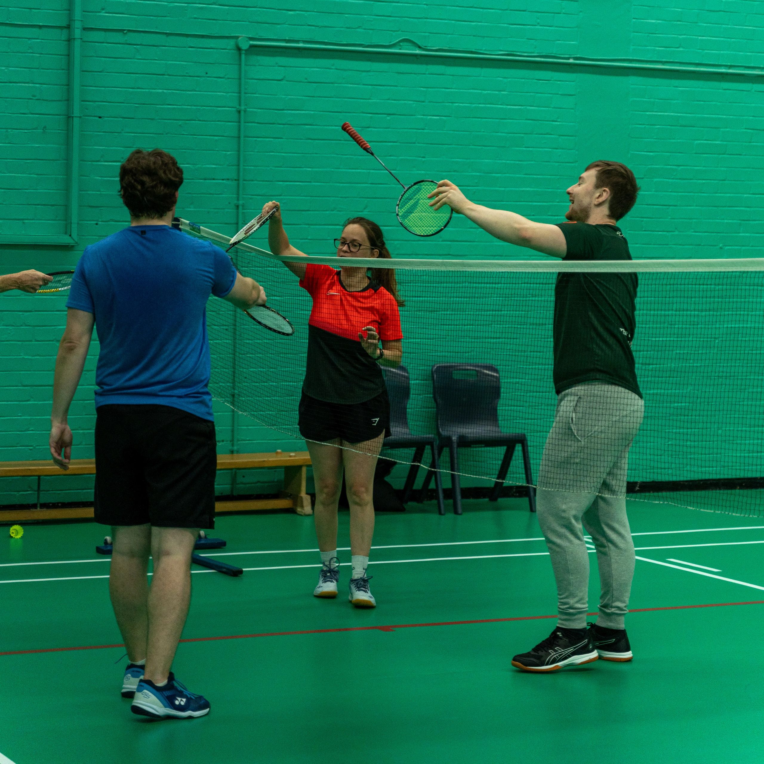 Four people playing badminton indoors, hitting the shuttlecock over the net.