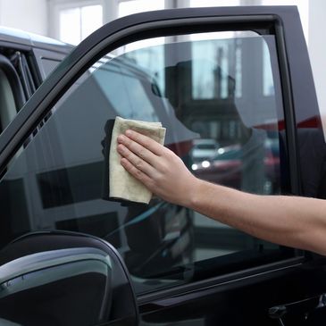 Hand cleaning a car window with a cloth inside a garage.