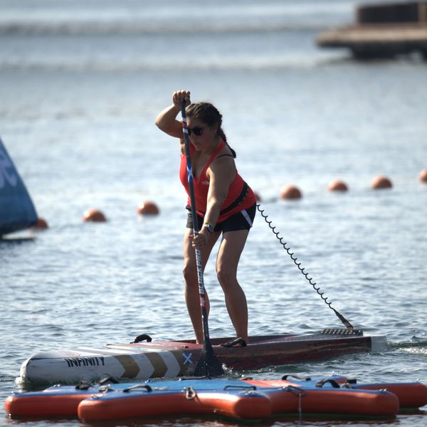 Woman paddleboarding on calm water wearing sunglasses and a red tank top.
