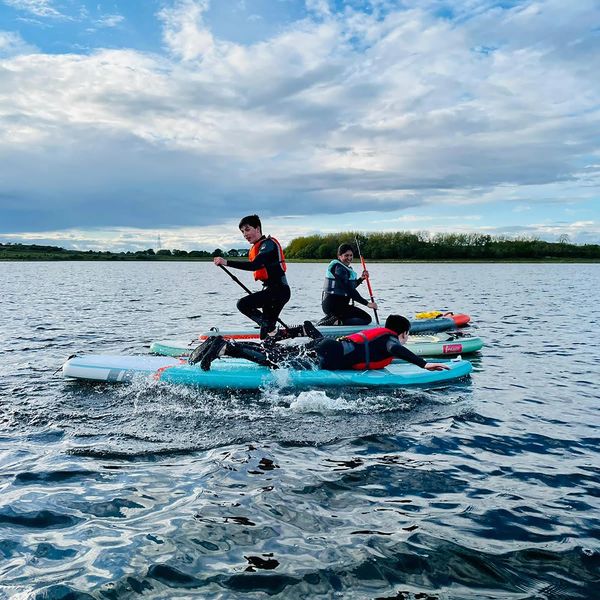 Three people paddleboarding on a lake under a partly cloudy sky.