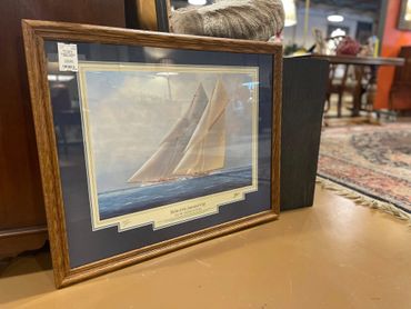 Framed painting of a sailing yacht on the water with a dark blue mat and gold frame.